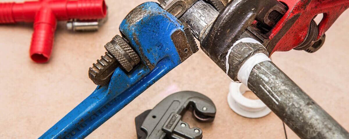 plumber using pipe wrench to repair plumbing pipe connection